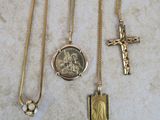 three gold necklaces with a cross and a medal on a marble surface
