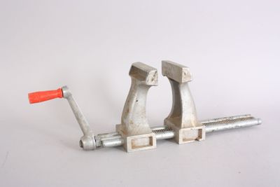 a metal clamp with a red handle on a white surface