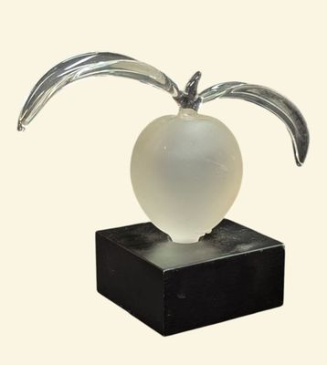 une sculpture en verre représentant une pomme posée sur un socle noir