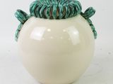 a white vase with a green decoration on top of it