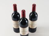three bottles of red wine sitting next to each other on a white surface