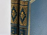 two blue books sitting on top of each other on a white surface