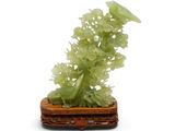 sculpture en jade représentant des fleurs et des feuilles, posée sur un socle en bois, sur fond blanc