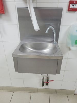 un lavabo en acier inoxydable dans des toilettes publiques, équipé d'un distributeur de serviettes en papier