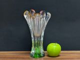 a green apple next to a glass vase on a table