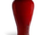 un vase rouge posé sur une surface blanche