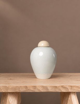 un vase blanc posé sur une table en bois, sur fond marron