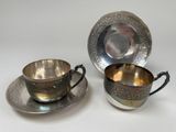 two silver plated cups and saucers on a white surface
