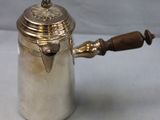 an antique silver coffee pot with a wooden handle on a table