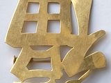 une broche en or sur laquelle figurent des caractères chinois sur un fond blanc