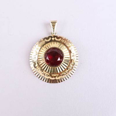 a close up of a gold pendant with a red stone