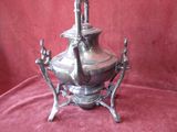 a silver tea pot on a stand on a red cloth
