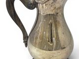 an old silver pitcher with a handle on a white surface