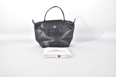 un sac à main noir avec un livre et un stylo sur fond blanc