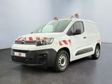 La camionnette blanche est garée dans une grande pièce ; elle porte une bande rouge et blanche sur le côté.