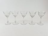 six clear wine glasses lined up in a row on a white surface