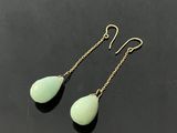 une paire de boucles d'oreilles vertes en forme de larme posées sur un fond noir