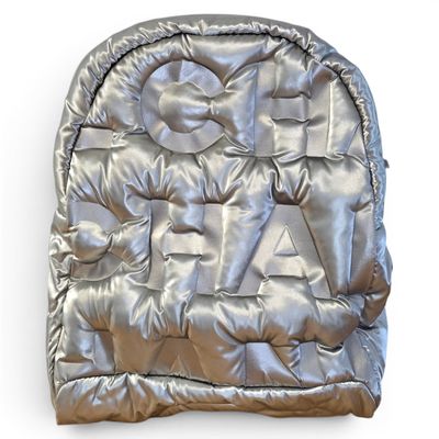 silver backpack with a bow tie on top of it on a white surface