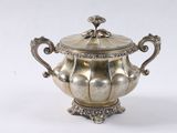 une théière ancienne en métal argenté, avec couvercle, posée sur un socle