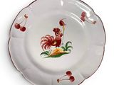 une assiette blanche sur laquelle est représenté un coq, avec des cerises à côté