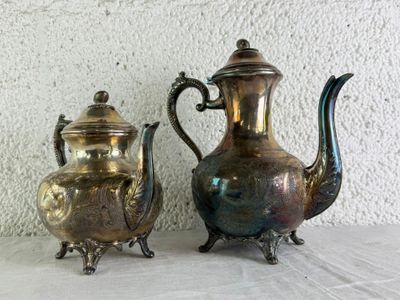 two silver teapots sitting next to each other on a table