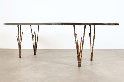 La table est fabriquée à partir de branches et possède un plateau noir.