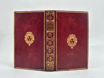 un vieux livre rouge avec des bordures dorées posé sur une surface blanche