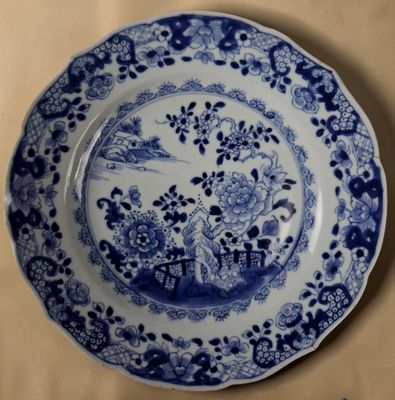une assiette bleue et blanche sur laquelle est représentée une femme dans un jardin