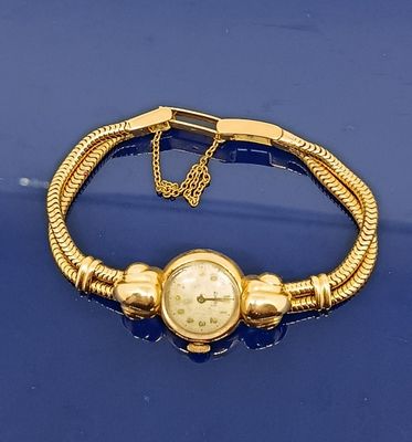 un bracelet en or sur lequel est fixée une montre, posé sur un fond bleu