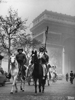 photographie en noir et blanc représentant des hommes à cheval devant l'Arc de Triomphe