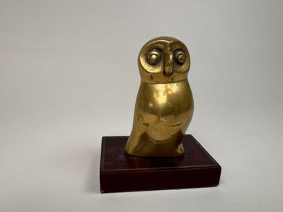 figurine en or représentant un hibou, posée sur un socle en bois, sur fond blanc