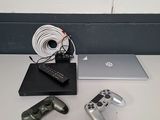 une table sur laquelle se trouvent un ordinateur portable, une manette de jeu et d'autres objets