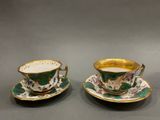 two cups and saucers with gold rims on a gray surface