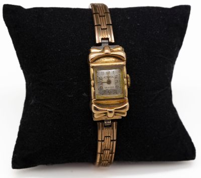 une photo d'une montre en or posée sur un coussin noir, elle-même posé sur un oreiller