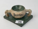 un petit bol en céramique posé sur un socle, sur lequel est accrochée une étiquette avec un nom