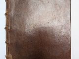 un vieux livre brun posé sur une table à côté d'un mur blanc
