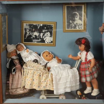 deux poupées dans une vitrine, avec des photos accrochées au mur