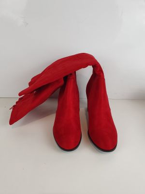 une paire de bottes en daim rouge posées sur une surface blanche, à côté d'une plante