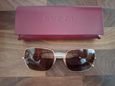 Lunettes de soleil Gucci et leur étui posés sur une surface en bois