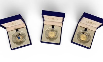 three gold coins are in a blue box on a white surface
