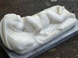 une statue représentant un bébé allongé sur un bloc de marbre