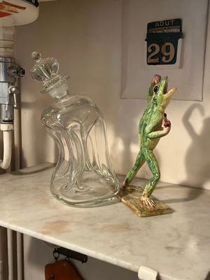 a frog figurine sitting on a shelf next to a glass bottle