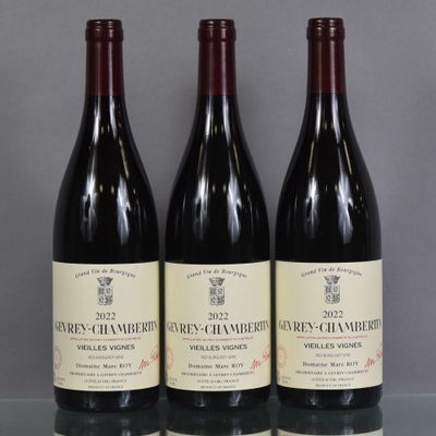three bottles of wine sit on a glass table in front of a gray wall