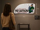 une femme debout devant un panneau sur lequel figure la photo d'un homme coiffé d'un haut-de-forme