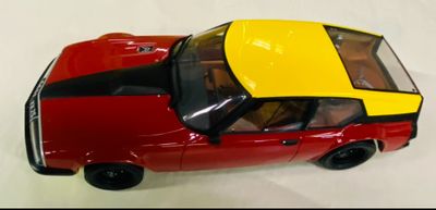 une petite voiture rouge avec un toit jaune posée sur une surface blanche