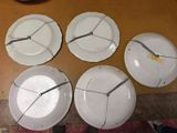 six white plates with a clock on them sitting on a table