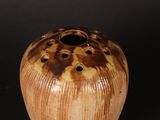 a brown vase with holes in it on a black surface