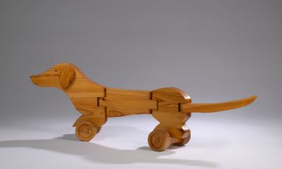 a wooden toy of a dog on wheels on a white surface