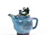 une théière bleue surmontée d'une petite figurine