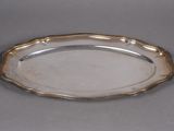 an antique silver plate with a decorative edge on a gray surface